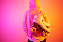 Person holding roller skates against a bright pink and orange background